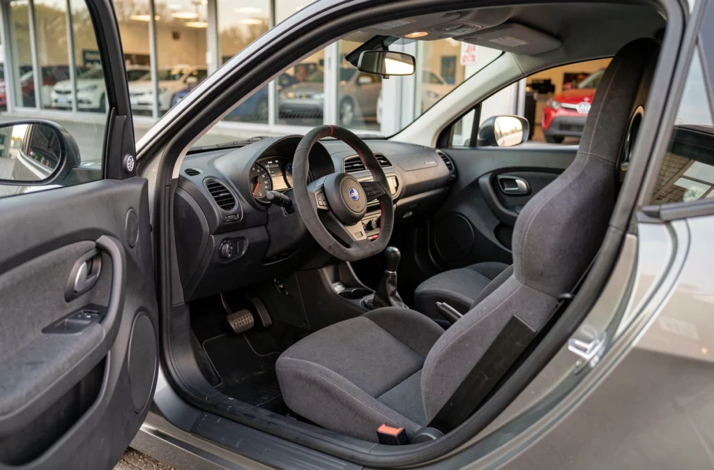 Intérieur de la Ligier JS50 Sport avec tableau de bord, volant et sièges baquets vus depuis la portière ouverte